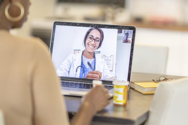 A patient speaks to a doctor through a video call on a laptop.