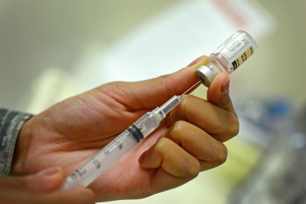 A hand injects a needle into a vial.