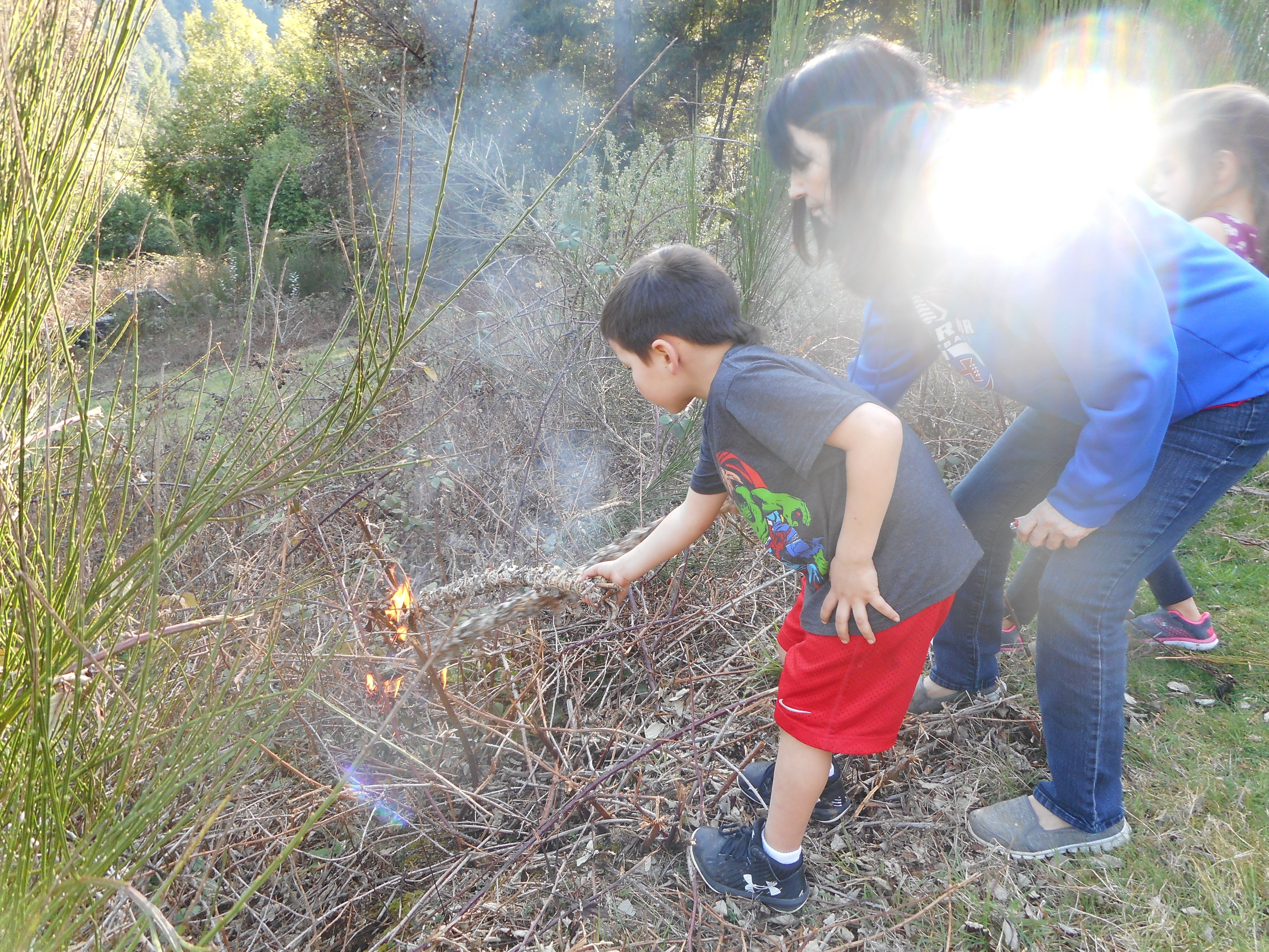 Margo Robbins (right), teaching her grandson, Joe Joe (left), how to culturally burn on Yurok land. 