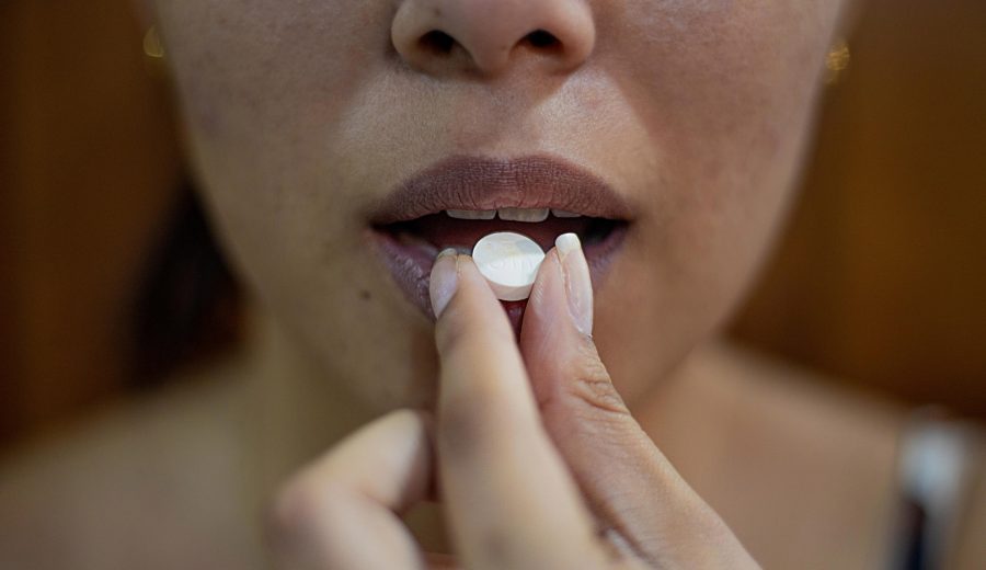A person holds a white pill up to their mouth.