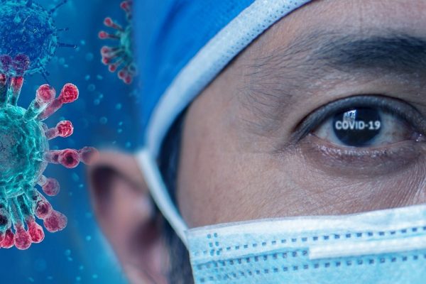 A medical professional in a mask in of an illustration of the coronavirus, with "COVID-19" typed onto the eye.